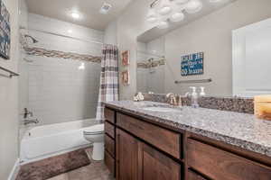 Full bathroom with vanity, a textured ceiling, shower / tub combo with curtain, tile patterned flooring, and toilet