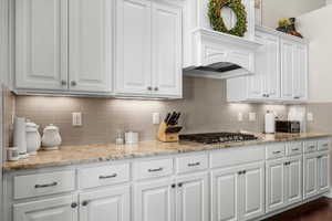 Kitchen with light stone countertops, dark hardwood / wood-style flooring, tasteful backsplash, stainless steel gas cooktop, and white cabinetry