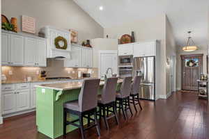 Kitchen with appliances with stainless steel finishes, dark hardwood / wood-style flooring, a kitchen island with sink, high vaulted ceiling, and white cabinets