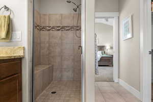 Bathroom featuring tile patterned flooring, a tile shower, vanity, and lofted ceiling