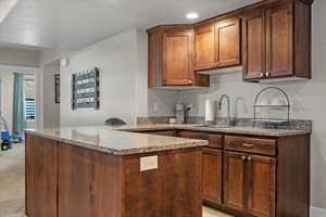 Kitchen featuring light stone counters, light colored carpet, kitchen peninsula, and sink