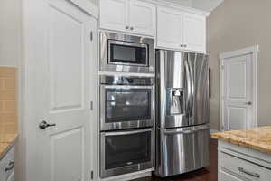 Kitchen with dark hardwood / wood-style flooring, stainless steel appliances, white cabinetry, and light stone counters