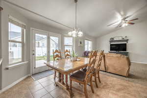 Dining room featuring ceiling fan with notable chandelier, vaulted ceiling, and light tile patterned flooring