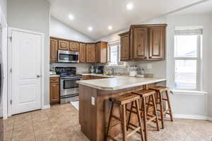 Kitchen featuring sink, stainless steel appliances, kitchen peninsula, vaulted ceiling, and a breakfast bar