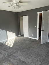 Unfurnished bedroom featuring dark colored carpet, a closet, and ceiling fan