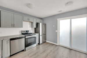 Kitchen featuring stainless steel appliances, light hardwood / wood-style flooring, tasteful backsplash, and gray cabinets