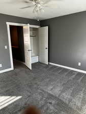 Unfurnished bedroom with a closet, dark carpet, and ceiling fan