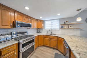 Kitchen featuring light wood-style floors, light stone countertops, sink, and appliances with stainless steel finishes, gas range, double oven.