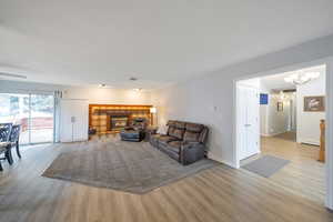 Living room with ceiling fan with notable chandelier, light wood-type flooring, baseboard heating, and a tile fireplace