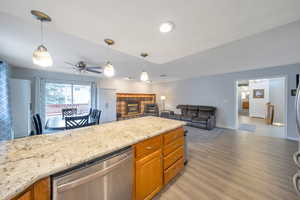 Kitchen featuring light stone countertops, a fireplace, ceiling fan, dishwasher, and light wood-style floors