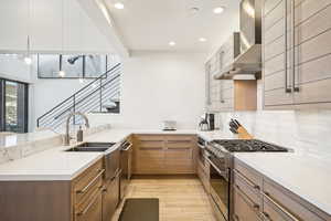 Kitchen featuring decorative backsplash, stainless steel appliances, wall chimney range hood, and light hardwood / wood-style floors