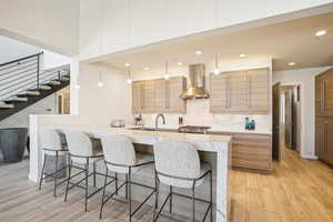 Kitchen featuring pendant lighting, a kitchen breakfast bar, wall chimney range hood, decorative backsplash, and light hardwood / wood-style floors