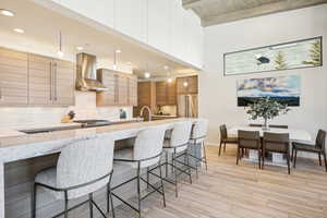 Kitchen featuring wall chimney exhaust hood, decorative light fixtures, a kitchen bar, decorative backsplash, and light wood-type flooring