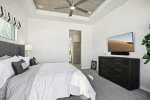 Bedroom featuring light carpet, a tray ceiling, ceiling fan, and ensuite bathroom