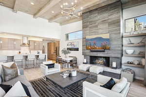 Living room featuring a tile fireplace, a chandelier, beamed ceiling, a high ceiling, and light hardwood / wood-style floors