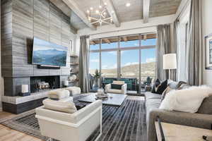 Living room with a tile fireplace, a high ceiling, an inviting chandelier, beamed ceiling, and hardwood / wood-style floors