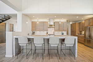 Kitchen featuring a kitchen bar, high end refrigerator, wall chimney exhaust hood, and light wood-type flooring