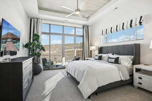 Bedroom featuring a raised ceiling, ceiling fan, carpet flooring, and access to outside