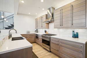 Kitchen featuring sink, wall chimney exhaust hood, backsplash, appliances with stainless steel finishes, and light wood-type flooring