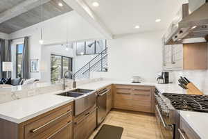 Kitchen with kitchen peninsula, appliances with stainless steel finishes, wall chimney exhaust hood, sink, and light hardwood / wood-style flooring