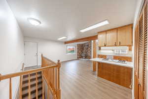 Kitchen with a wood stove, white gas stovetop, brick wall, light hardwood / wood-style floors, and a textured ceiling