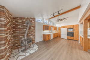 Kitchen with ceiling fan, lofted ceiling with beams, brick wall, white appliances, and light wood-type flooring