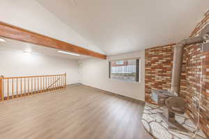 Unfurnished living room featuring vaulted ceiling with beams, a wood stove, brick wall, and hardwood / wood-style flooring