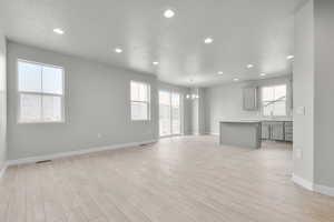 Unfurnished living room featuring a notable chandelier, light hardwood / wood-style floors, sink, and a textured ceiling