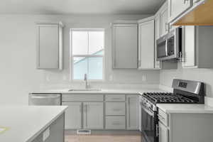 Kitchen with sink, appliances with stainless steel finishes, gray cabinetry, and light hardwood / wood-style flooring