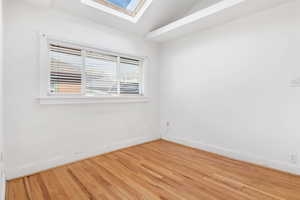 Spare room with lofted ceiling with skylight and hardwood / wood-style floors