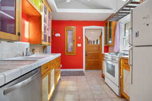 Kitchen with backsplash, tile counters, light tile patterned flooring, and white appliances