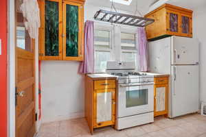 Kitchen with white appliances, light tile patterned floors, and a skylight