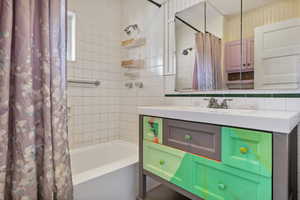 Bathroom featuring vanity, tile walls, shower / tub combo, and tasteful backsplash