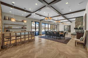 Dining area featuring a chandelier, beam ceiling, light parquet flooring, and indoor bar