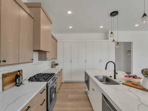 Kitchen with a sink, light wood-type flooring, modern cabinets, light stone counters, and appliances with stainless steel finishes