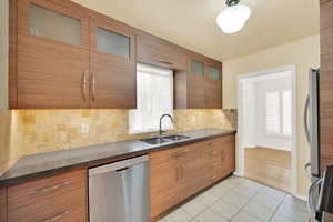 Kitchen featuring light tile patterned flooring, stainless steel appliances, tasteful backsplash, and sink