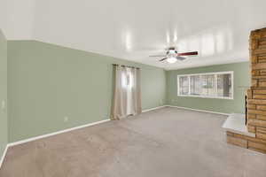 Unfurnished living room featuring ceiling fan, light colored carpet, lofted ceiling, and a fireplace