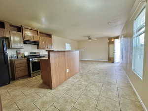 Kitchen featuring ceiling fan, stainless steel stove, light tile patterned floors, black fridge, and a kitchen island