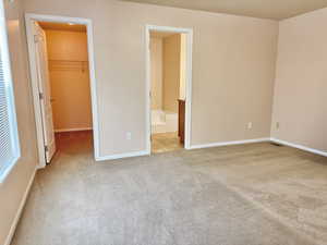 Unfurnished bedroom featuring a walk in closet, ensuite bathroom, a closet, and light colored carpet