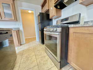 Kitchen with light stone countertops, black fridge, gas range, light tile patterned floors, and range hood