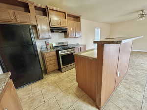 Kitchen featuring a center island, stainless steel gas range oven, black fridge, ceiling fan, and light tile patterned floors