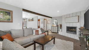 Carpeted living room featuring beamed ceiling, a textured ceiling, and a fireplace