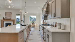 Kitchen featuring custom exhaust hood, decorative light fixtures, sink, and a large island with sink