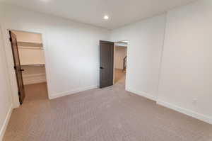 Unfurnished bedroom with a walk in closet, light carpet, and a closet