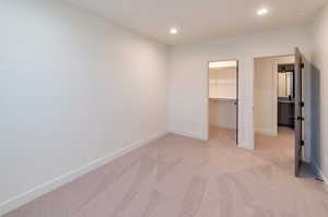 Unfurnished bedroom featuring light colored carpet, a walk in closet, and a closet