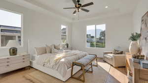 Bedroom with light wood-type flooring, a tray ceiling, and ceiling fan