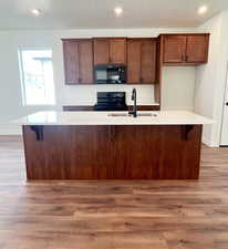 Kitchen with black appliances, light hardwood / wood-style floors, and an island with sink