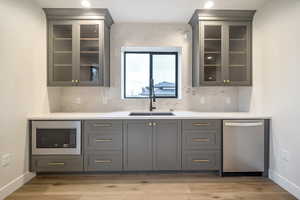 Bar featuring tasteful backsplash, light hardwood / wood-style floors, stainless steel appliances, sink, and gray cabinets