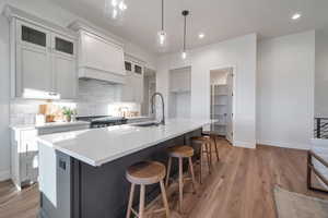 Kitchen with sink, an island with sink, hanging light fixtures, and light hardwood / wood-style flooring