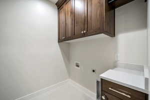 Washroom with cabinets, hookup for a washing machine, light tile patterned floors, and electric dryer hookup